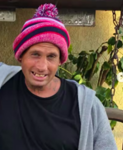 A white transgender woman in a pink hat smiles at the camera