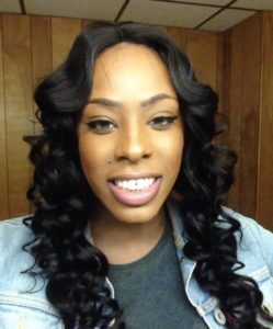 black transgender woman with dark wavy hair smiles at the camera