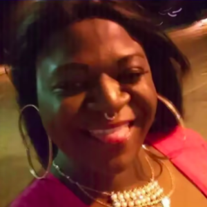 a black transgender woman with large hoop earrings grins at the camera
